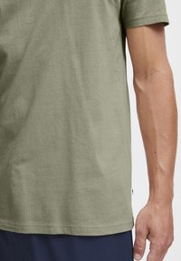 Olive green short-sleeve t-shirt made of soft cotton, featuring a straight hemline and subtle stitching details. Worn with navy pants.