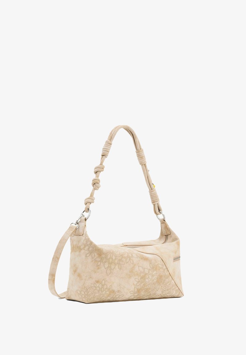 Bež torba s urezanim cvjetnim uzorcima, s detaljima u čvoru na naramenici i srebrnim ukrasima na patent zatvaraču.