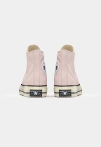 Rosa høye sneakers laget av canva med hvite detaljer, en rund logo-patch og svarte stripete gummisåler. Bakside vist.