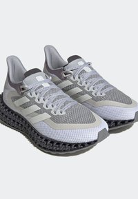 Zapatillas deportivas grises con parte superior de malla, acentos texturizados y una suela negra con un patrón distintivo. Presenta tres rayas blancas y cordones grises.