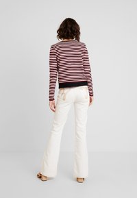 Randig långärmad topp i vinröd och krämfärgad, med ett svart midjeband. Vita utsvängda jeans med ljus broderi på fickorna.