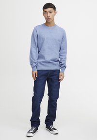 Pulover cu guler rotund de culoare albastru deschis, realizat dintr-un material moale, asortat cu blugi de culoare albastru închis și adidași negri și albi. Design simplu și casual.