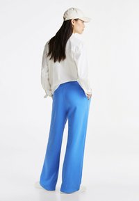 Niebieskie spodnie szerokie i biała koszula z kołnierzykiem, w zestawie z beżową czapką z daszkiem. Spodnie mają kieszenie i są wykonane z gładkiego materiału.