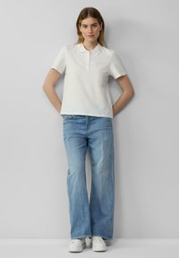 Witte polo met korte mouwen en een knoopsluiting, gecombineerd met lichtblauwe wijde jeanstukken en witte sneakers. Eenvoudige, casual stijl.