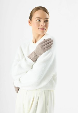 Gants tricotés en taupe clair avec des poignets côtelés, ornés d'un motif floral brodé. Portés avec un pull blanc confortable.