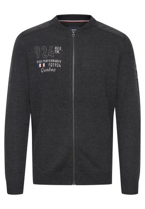 Tamsiai pilkas zip-up megztinis su gurgurančiomis rankovėmis ir apatine dalimi. Yra siuvinėtas tekstas ir logo ant krūtinės, taip pat oda primenanti detalė ant pečių.