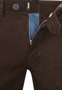Bruine broek met een rits, voorzien van een lichtblauwe voering. De stof lijkt soepel met zichtbare stiksels en een knoopsluiting.