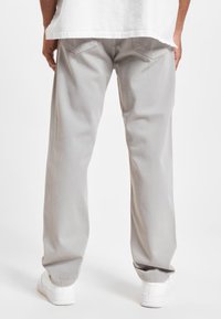 Light gray straight-leg pants made of cotton denim with a smooth texture, featuring two back pockets and cuffed hems. Styled with white sneakers.
