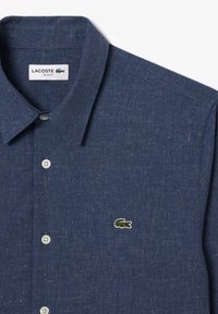 Camisa ajustada de botones en azul marino, hecha de una tela texturizada, con un collar puntiagudo y un pequeño logo bordado de Lacoste en verde en el pecho.