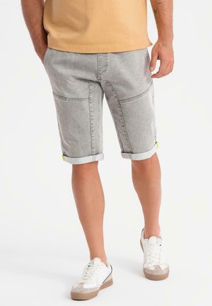 Shorts en denim gris avec ourlets retroussés, présentant des poches latérales et des accents verts. Associés à des baskets blanches, affichant un look décontracté.