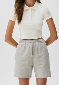 Afgeknipt wit poloshirt met een geribbelde textuur en een knoopsluiting, gecombineerd met lichtgrijze shorts met een elastische tailleband en een trekkoord.