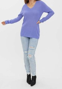 V-kaula-aukollinen violetti ribbineulottu pusero, pitkät hihat, yhdistetty vaaleansinisiin revittyihin skinny-farkkuihin ja mustiin nilkkureihin. Sileä pinta, rento istuvuus.