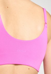 Rozā sporta krūšturis ar ribotu tekstūru, ar plānām siksniņām un vārdu "SPĒCĪGĀKS" izspiestu uz lentas. Vienkāršs dizains un bezšuvju malas.