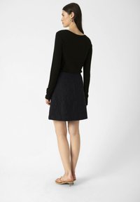 Haut noir à manches longues associé à une jupe noire texturée. La jupe a une taille ajustée et s'évasent légèrement au niveau de l'ourlet.