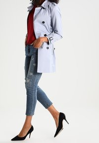 Světle modrý trenčkot s tmavými knoflíky, nošený přes červený top, spárovaný s roztrhanými džíny a černými vysokými podpatky.