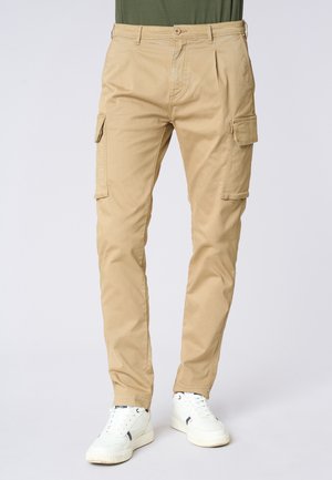 Pantaloni cargo beige in cotone, con tasche laterali, chiusura con bottone e gamba affusolata. Indossati con sneakers bianche.