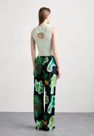 Top sin mangas de color verde claro con textura acanalada y un corte circular, combinado con pantalones negros holgados que presentan patrones de plantas coloridos.