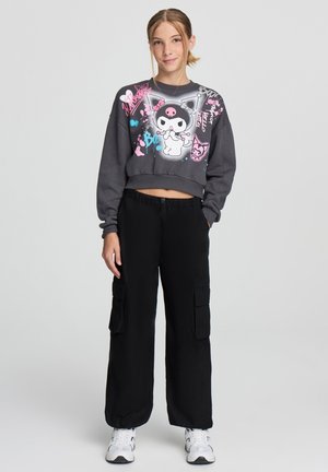 Felpa grigia a maniche lunghe con design grafici colorati, abbinata a pantaloni cargo neri con tasche laterali e una vestibilità comoda.