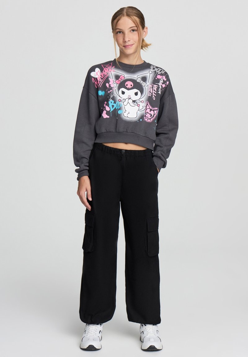 Wyciety szary sweter z kolorowymi grafikami, w połączeniu z czarnymi spodniami cargo z bocznymi kieszeniami i luźnym krojem.