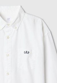 Balta vaikų marškinėlių su sagomis su kairiosios krūtinės kišene, išsiuvinėta mėlynomis raidėmis „GAP“.