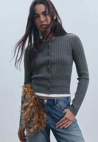 Siv ribani kardigan s krožnim izrezom in gumbnim zapiranjem, v kombinaciji z jeansa iz denima, ki imajo podrobnost iz umetnega krzna na bokih.