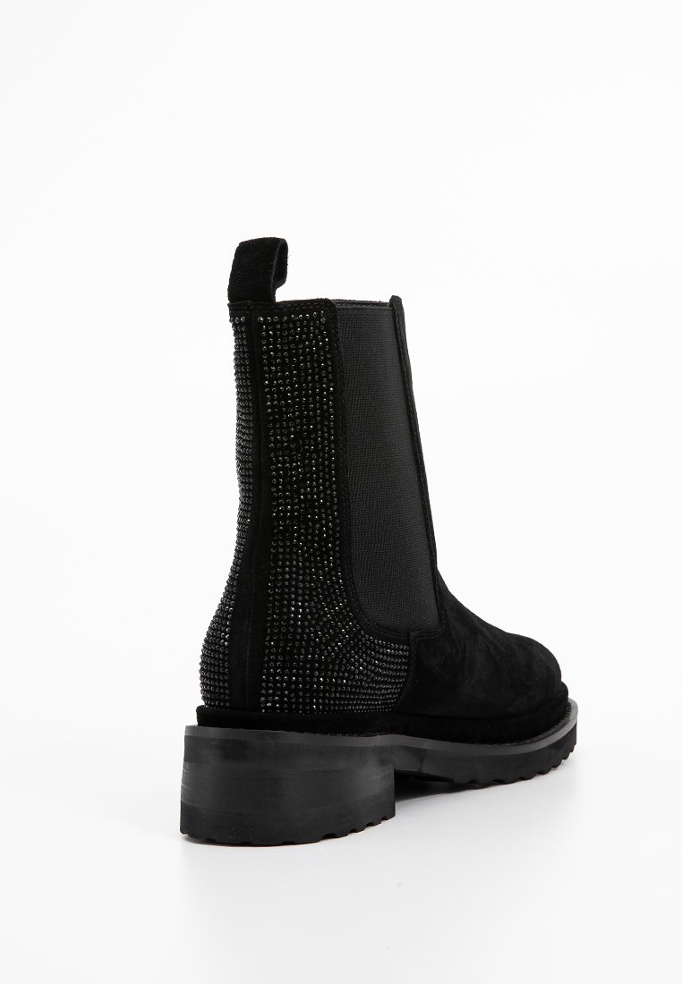 Bottines noires en suede et tissu, avec un dos clouté, des côtés élastiques et une semelle en caoutchouc noir épaisse.