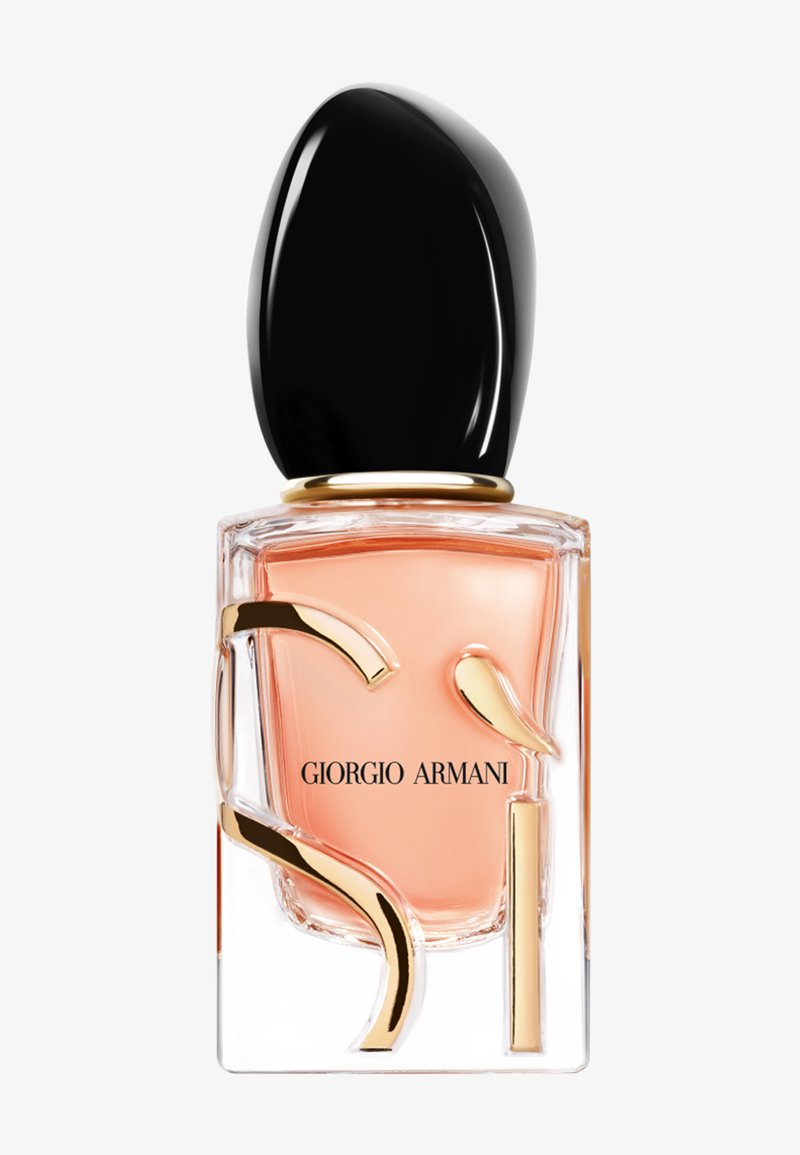 Przezroczysta prostokątna butelka perfumu z brzoskwiniowym płynem, czarną asymetryczną nakrętką, złotymi dekoracyjnymi akcentami i napisem "Giorgio Armani" na przodzie.
