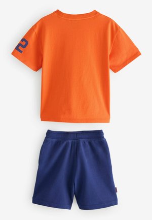 Kurzes, orangefarbenes T-Shirt aus Baumwolle mit der blauen Zahl "2" am Ärmel, kombiniert mit marineblauen Shorts mit elastischem Bund.