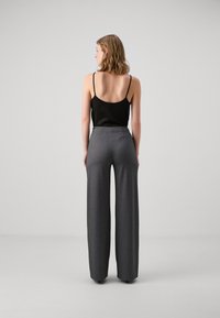 Top nero con spalline sottili e pantaloni grigi a vita alta e gamba larga, con una texture liscia, mostrati di schiena su uno sfondo neutro.