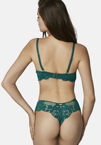 Ensemble bralette et thong en dentelle turquoise avec de délicats motifs floraux, des bretelles réglables et des bords festonnés. Elle présente une fermeture à crochets dans le dos.