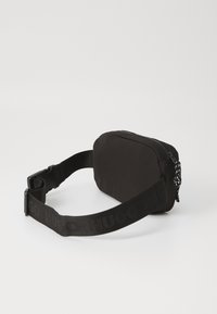 Sac ceinture en nylon noir de forme rectangulaire, doté d'une fermeture éclair, d'une sangle ajustable et d'un logo en relief sur la sangle.