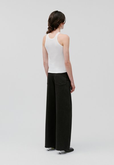 Top alb fără mâneci, cu bretele late, asociat cu pantaloni negri, lejeri, care au buzunare frontale și o finisare mată. Textură netedă și design casual.