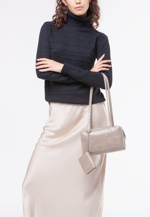Maglione nero a coste con collo alto, gonna in satin beige e borsa in tessuto leggero grigio chiaro con un portafoglio piccolo abbinato. Tessuti lisci e sofisticati.
