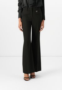 Fekete, testhezálló, bővülő szárú nadrág magas derékkal, ezüst négyzet alakú csattal és sima textúrával, fekete, pántos magas sarkú cipővel párosítva.