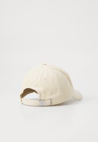 Beige corduroy cap with a curved brim, adjustable strap at the back, and subtle logo accent. Textured fabric with visible ribbed pattern.