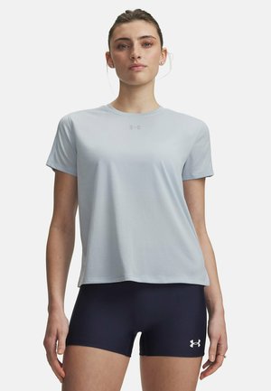 Vrouw draagt lichtblauw sportshirt met korte mouwen en donkerblauwe aansluitende korte broek, staand tegen een effen achtergrond.