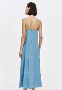 Jeans-Maxikleid mit verstellbaren Spaghettiträgern, einem gestuften Design und einer hellblauen Farbe. Mit einem rückenfreien Stil und fließender Textur.