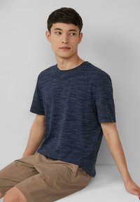 Marineblauwe t-shirt met korte mouwen in een gestructureerde stof en een ronde hals, gecombineerd met beige shorts. Eenvoudig, casual ontwerp.