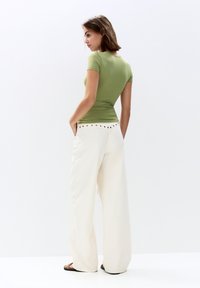 Tricou ajustat de culoare verde măsliniu, asortat cu pantaloni largi de culoare crem cu talie înaltă, care au un detaliu decorativ cu nasturi.