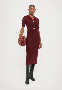 Maroon striped midi dress with a collared neck, short sleeves, and a fitted silhouette. Paired with a red bag and tall black boots.