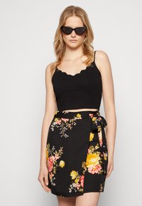 Top preto cortado com decote em scallop, combinado com uma saia envolvente floral com flores amarelas e rosas sobre um fundo preto.