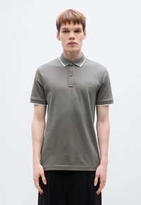 Γκρι πόλο μπλούζα με λευκό περίγραμμα στον γιακά και τα μανίκια. Διαθέτει μικρό λογότυπο στο αριστερό στήθος και κλασικό σχέδιο με κουμπιά στο μπροστινό μέρος.