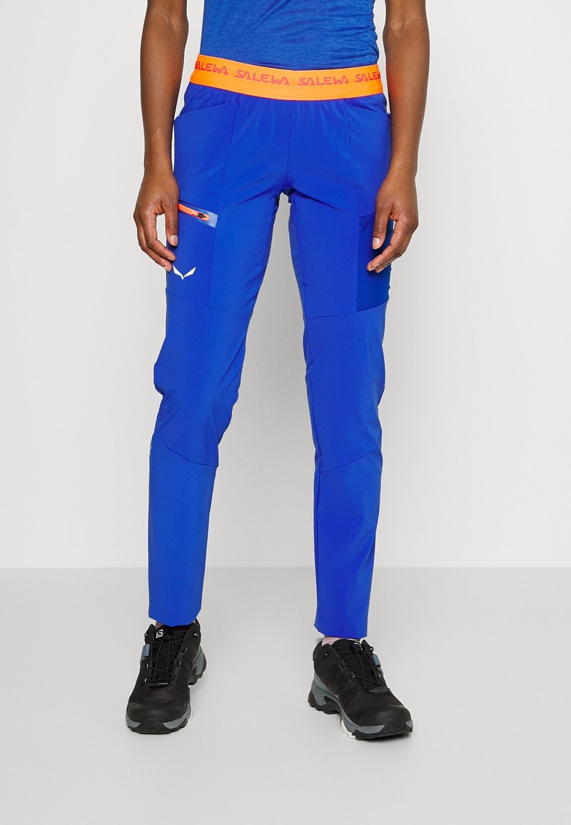 Siniset ulkoiluhousut, joissa on oranssi vyötärö, useita taskuja ja slim fit -muotoilu. Valmistettu kevyestä, kestävästä materiaalista, joka soveltuu vaeltamiseen.