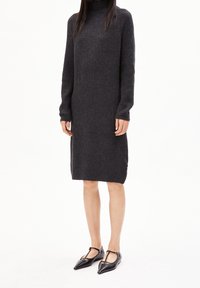 Robe en maille côtelée grise avec manches longues, col montant et fente latérale. Portée avec des ballerines noires à bout pointu et lanières autour de la cheville.