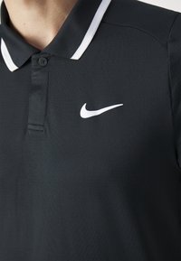Juodas polo marškinėliai su tekstūruotu audiniu, balta juostelė ant apykaklės ir mažas baltas Nike logotipas kairėje krūtinės pusėje. Su mygtukais.