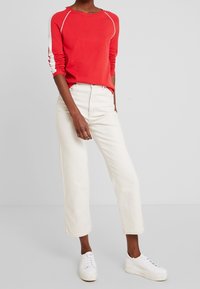 Maglione lungo rosso con strisce bianche, abbinato a jeans dritti a vita alta color avorio e sneaker bianche.