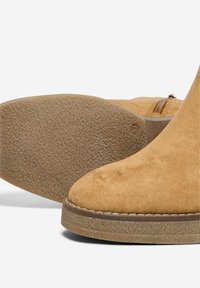 Bottines en nubuck couleur tan avec une semelle en caoutchouc texturé. Caractéristiques : un bout arrondi et des détails légèrement cousus le long de la semelle.