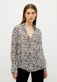 Blusa ligera y transparente en beige con patrones florales en azul marino. Cuenta con un collar clásico, cierre de botones en la parte delantera y mangas largas con detalle en los puños.