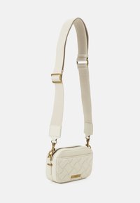 Piccola borsa a tracolla trapuntata color crema con cinghia in tessuto regolabile e hardware in metallo color oro su sfondo bianco.
