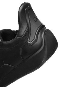 Nahaufnahme der Ferse eines schwarzen Sneakers, die die strukturierte Sohle, genähtes Leder und synthetische Überzüge mit geprägtem Logo-Detail zeigt.